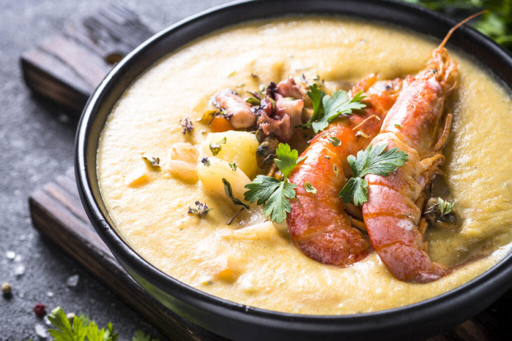 Grits topped with a lobster tail, shrimp, and sausage, all covered in garlic butter sauce.