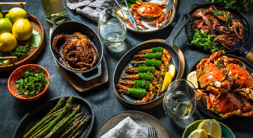 A black tabletop holding several seafood dishes topped with different sauces