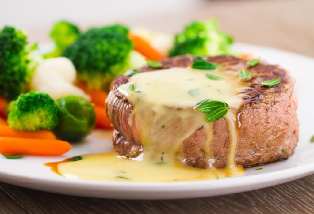 A grilled beef filet topped with sauce and vegetables on the side.