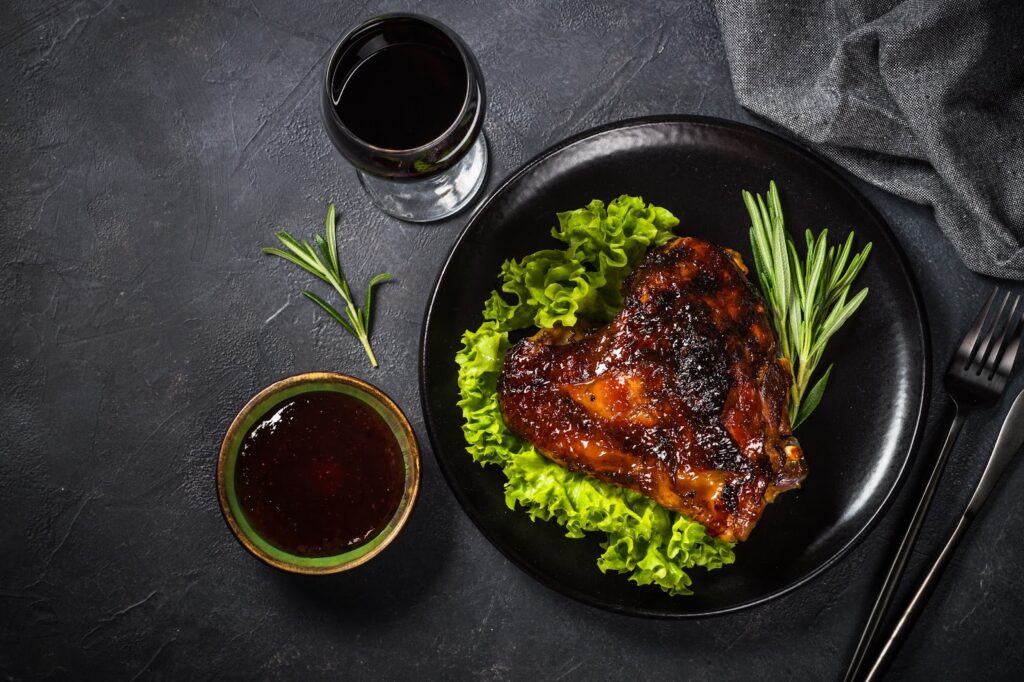 A baked turkey thigh with a side of dark sauce and herbs.