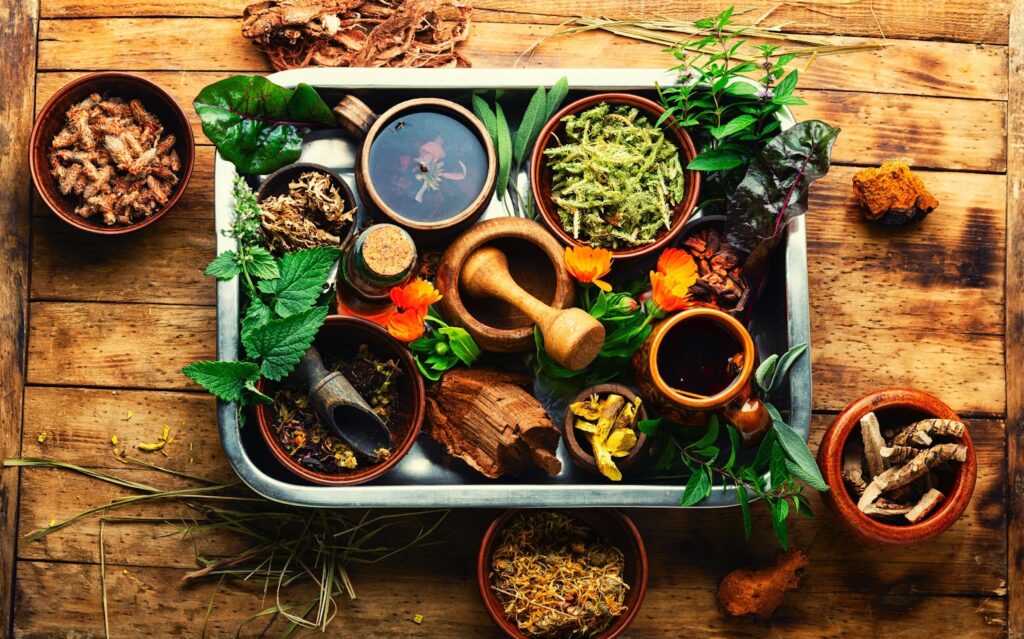 A tray full of different herbs arranged in bowls. The tray rests on an old wooden table.