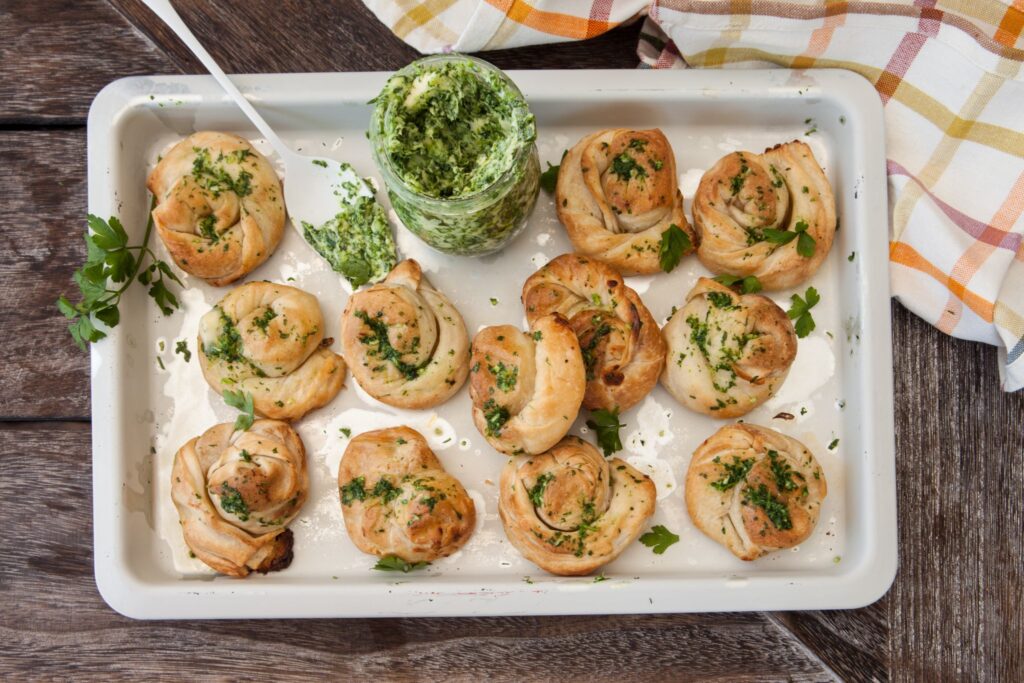 A tray full of garlic knots with a jar of garlic butter sauce.