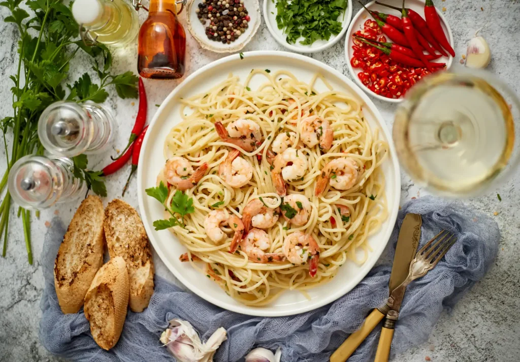 Spaghetti with shrimp in a white sauce on a white ceramic plate and served with a glass of white wine.