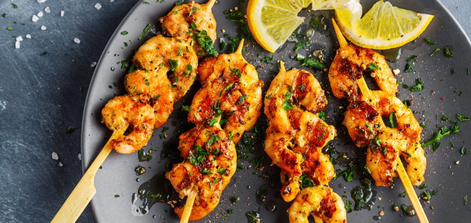 Three shrimp skewers served on a plate with lemon slices.