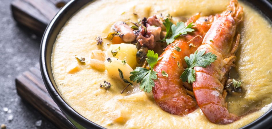 Grits topped with a lobster tail, shrimp, and sausage, all covered in garlic butter sauce.