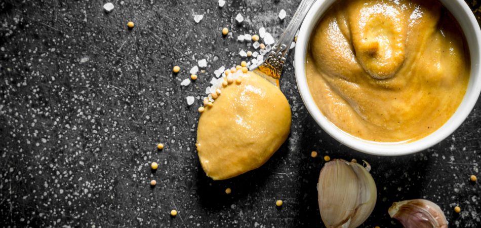 A homemade garlic butter sauce in a bowl against a marble background. There are cloves of garlic in the background.