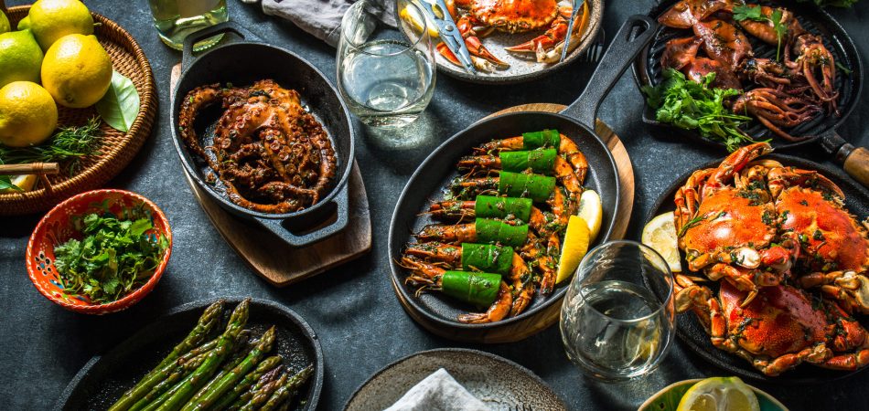 A black tabletop holding several seafood dishes topped with different sauces