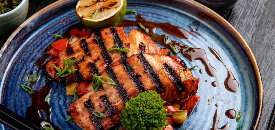 A ceramic plate holding grilled salmon topped with salsa, guacamole, and other dressings.