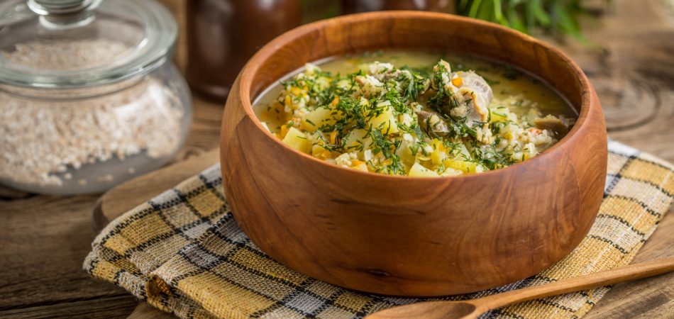 A barley and chicken soup with garlic served in a wooden bowl with a wooden spoon.